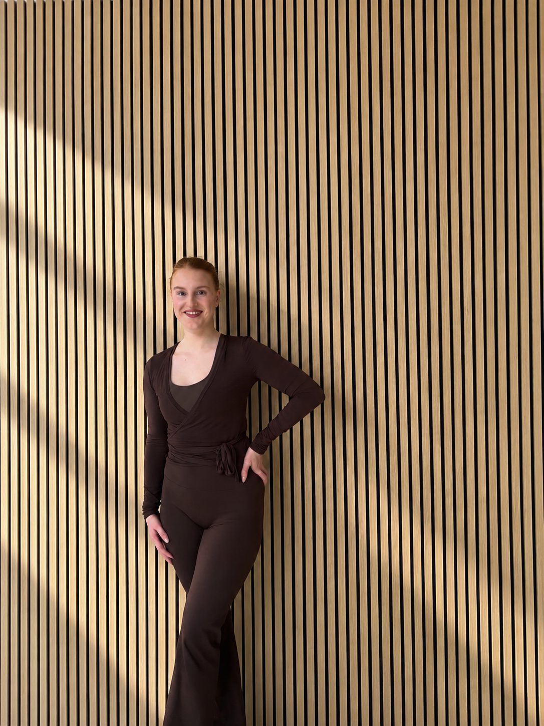 Selina lächelnd vor der Holzlamellenwand im Studio