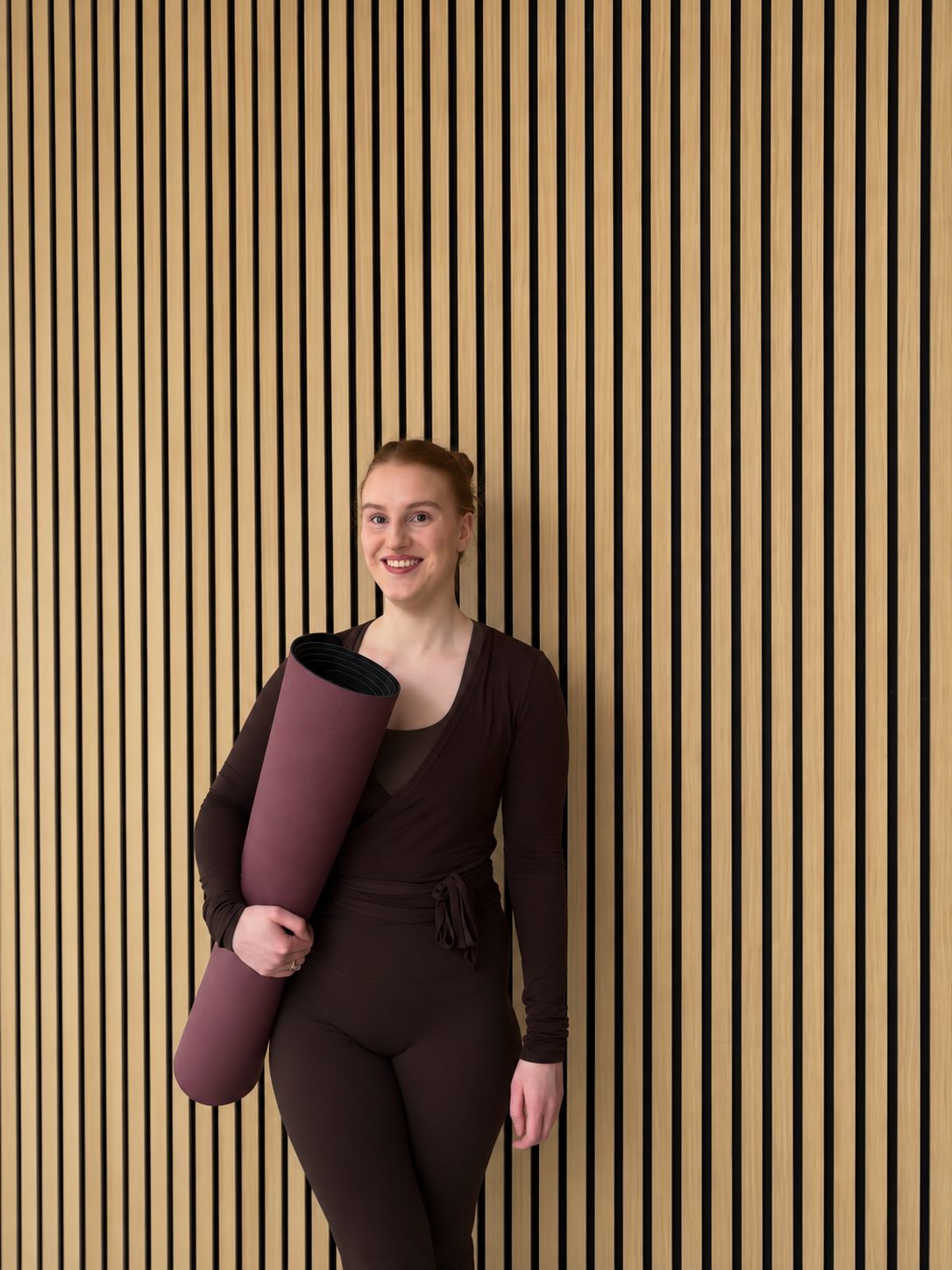 Selina mit Yogamatte vor der Holzwand