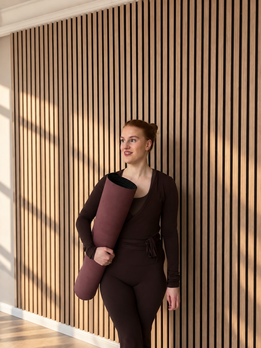 Mit Yogamatte im Arm vor der Holzwand